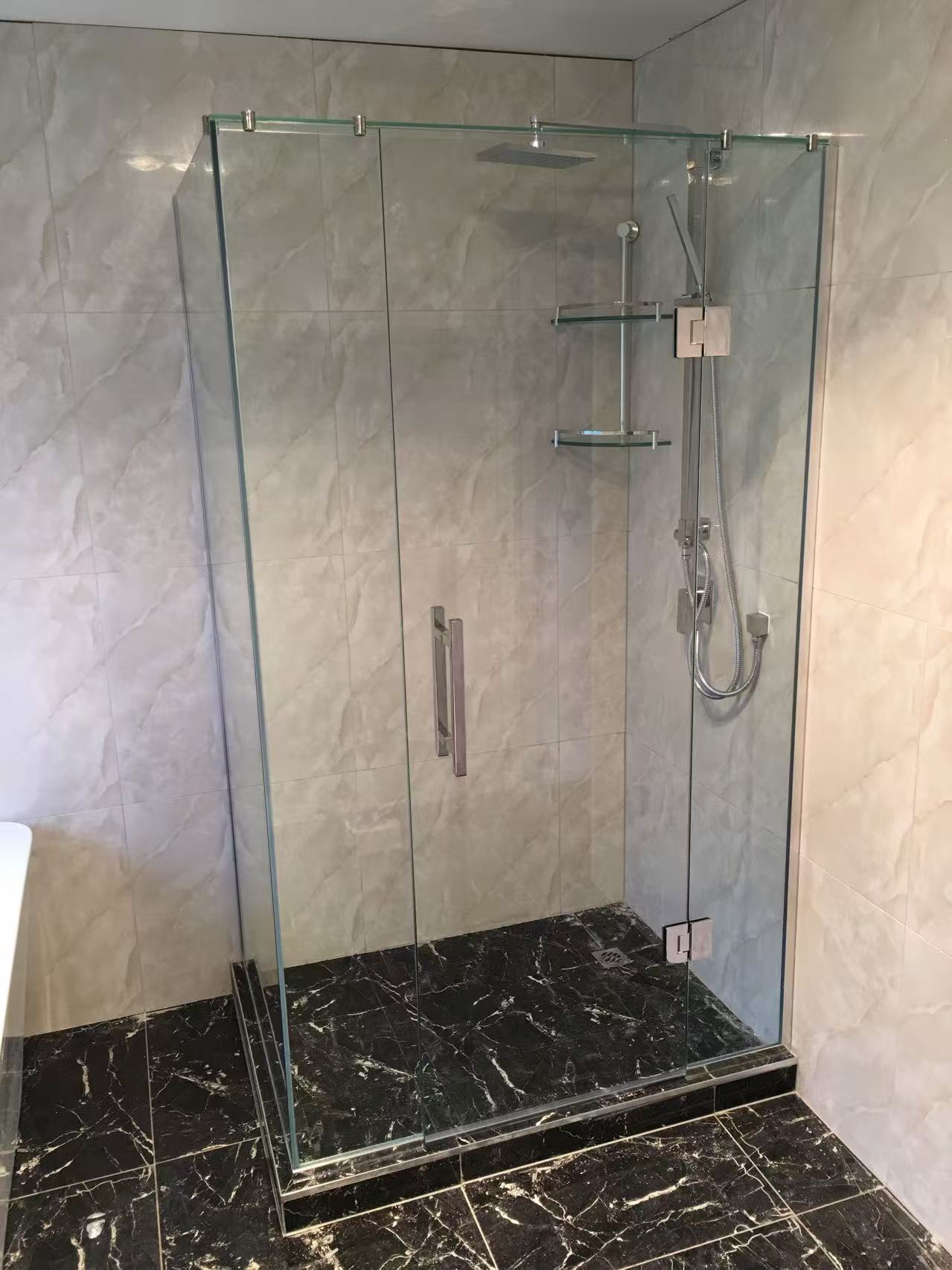Frameless shower enclosure with chrome hardware and dark marble floor