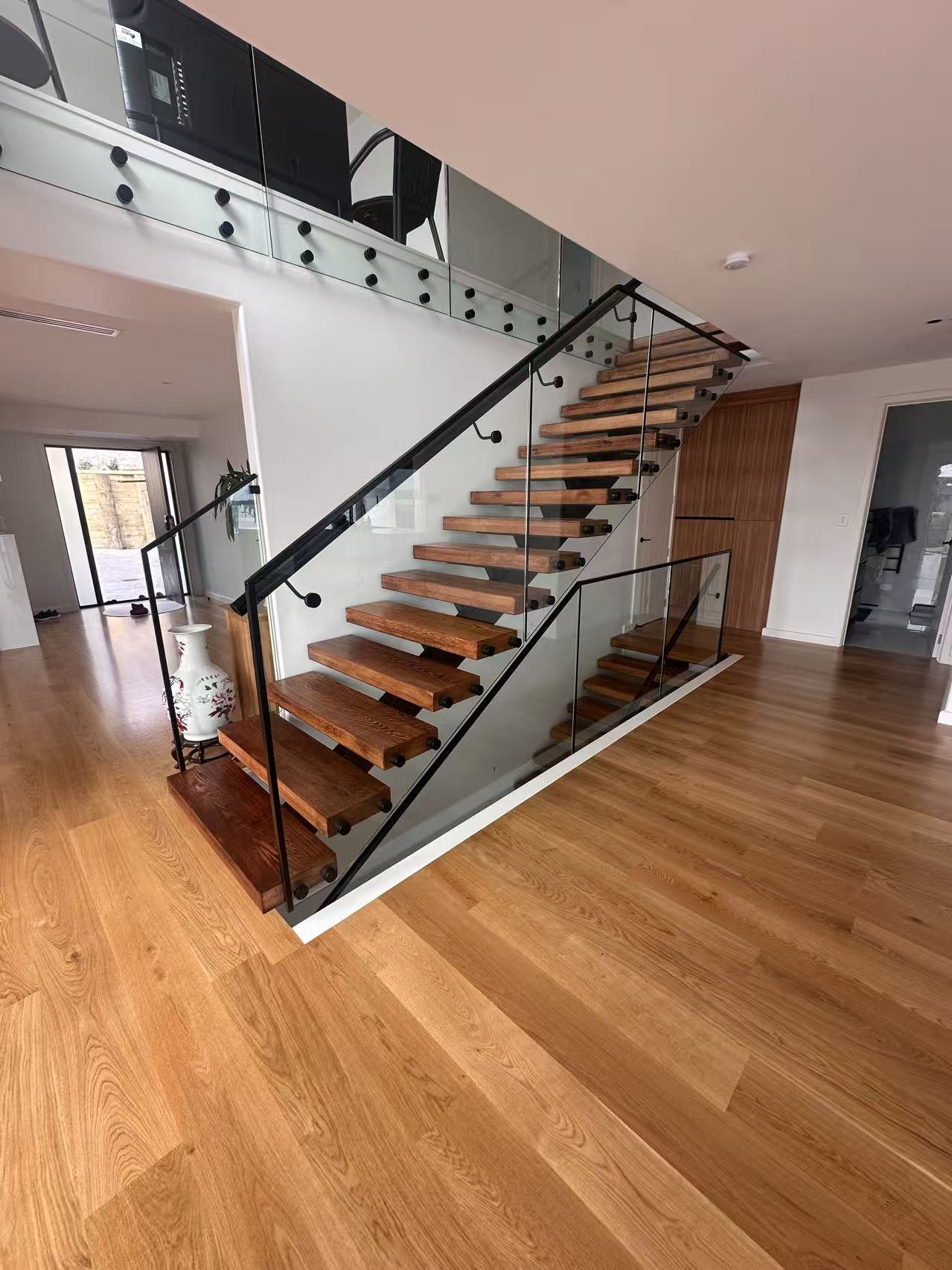 Wide view of a floating timber staircase with glass balustrades and black handrails